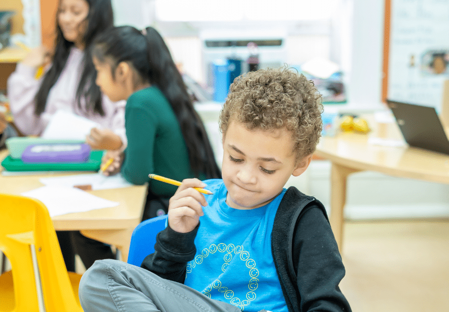 Young boy holding a pencil in a classroom