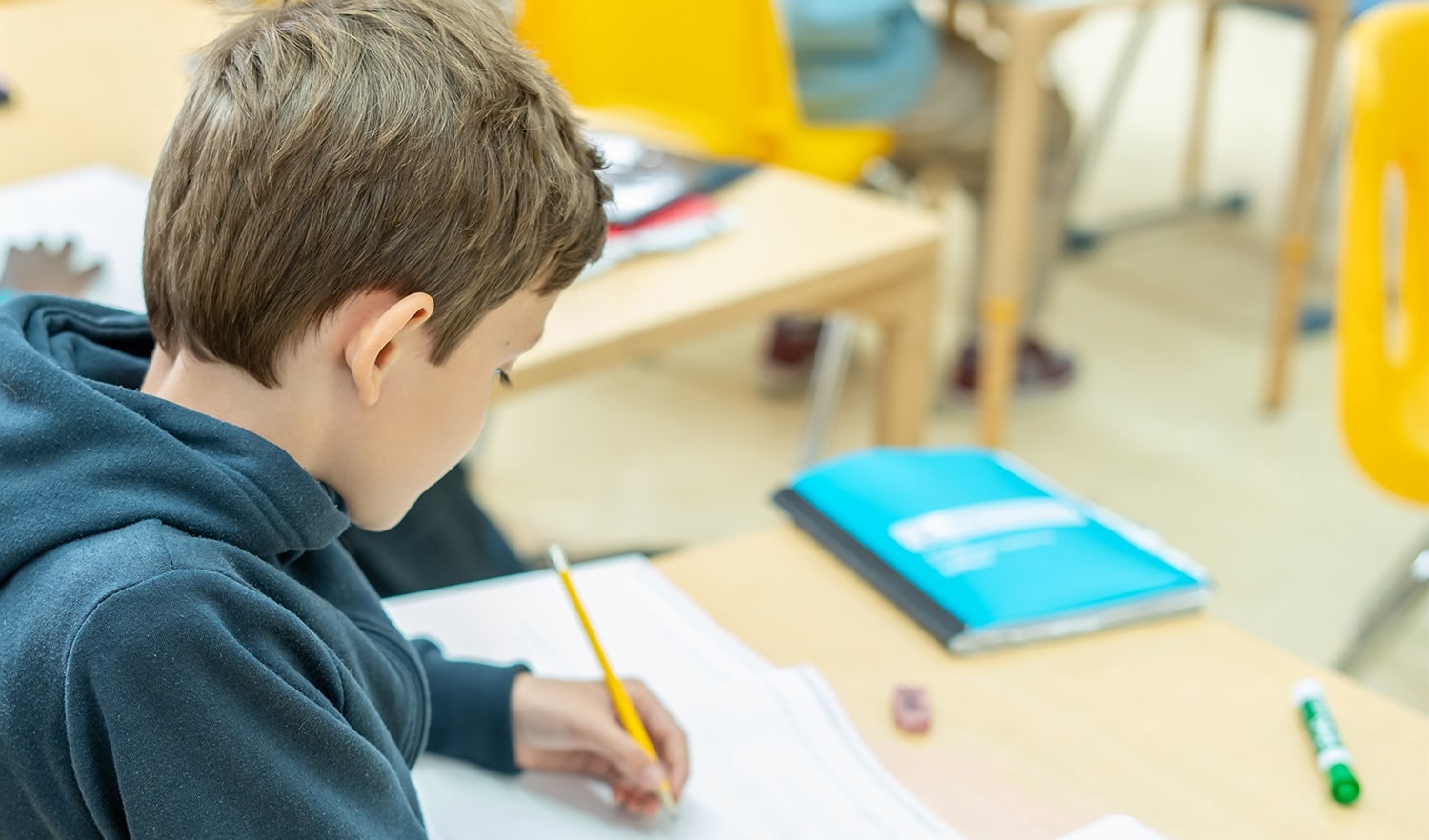 young boy at desk writes with a pencil